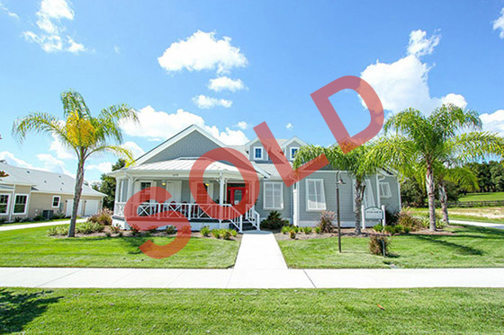 Front view of a gray two-story home with a white porch and palm trees, overlaid with a red SOLD stamp.