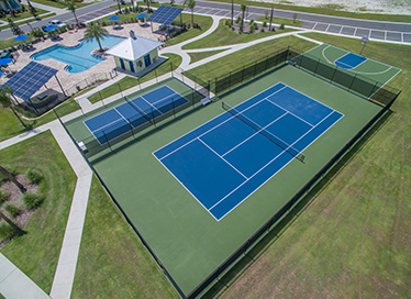 Aerial view of blue and green tennis courts with solar panels on the roof of a nearby building.