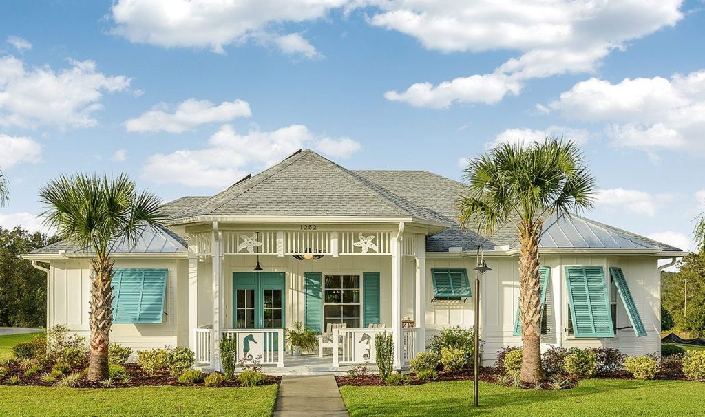 Cream coastal home with teal shutters, seahorse porch accents, palm trees, and metal roof under blue sky.