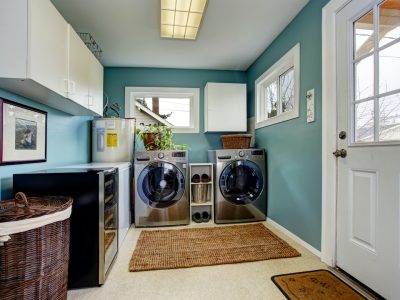 Laundry room with teal walls, white cabinets, stainless steel washer and dryer, and a wicker laundry basket.