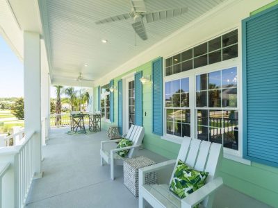 Spacious front porch with white Adirondack chairs, blue shutters, and a ceiling fan overlooking a green lawn.