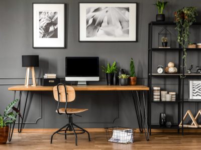 Modern home office with a wooden desk, black shelving unit, and framed botanical art on a gray wall.