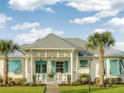 Cream coastal home with teal shutters, seahorse porch accents, palm trees, and metal roof under blue sky.