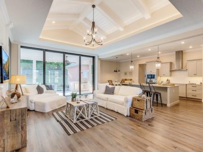 Open concept living room with white furniture, wood floors, and a view of the kitchen and sliding glass doors.