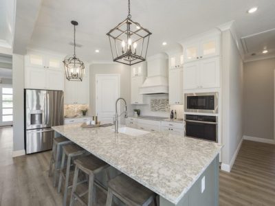Modern kitchen with white cabinets, granite island, stainless steel appliances, and geometric light fixtures.