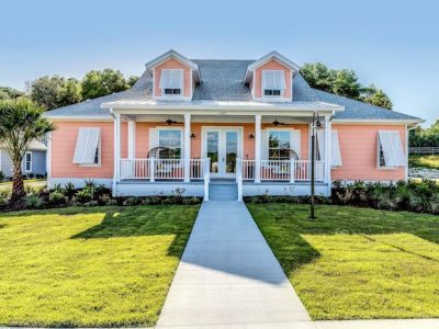 Front view of a peach-colored single-story home with a white front porch, gray shingle roof, and two dormer windows.