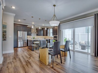 Islamorada model dining room with glass table, dark chairs, and view of kitchen with stainless steel appliances and wood f...
