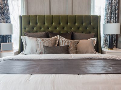 Bedroom with a large green tufted headboard, layered pillows, and matching nightstands with lamps.