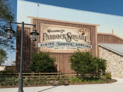 Mural on a building wall reads Welcome to Paddock Square Dining Shopping Dancing, featuring rustic wood and stone textures.